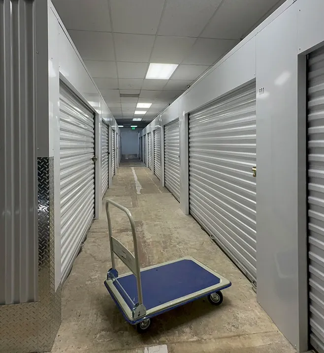 Inside hallway of Ken's Korner Mini Storage with units on each side with cart in the middle.